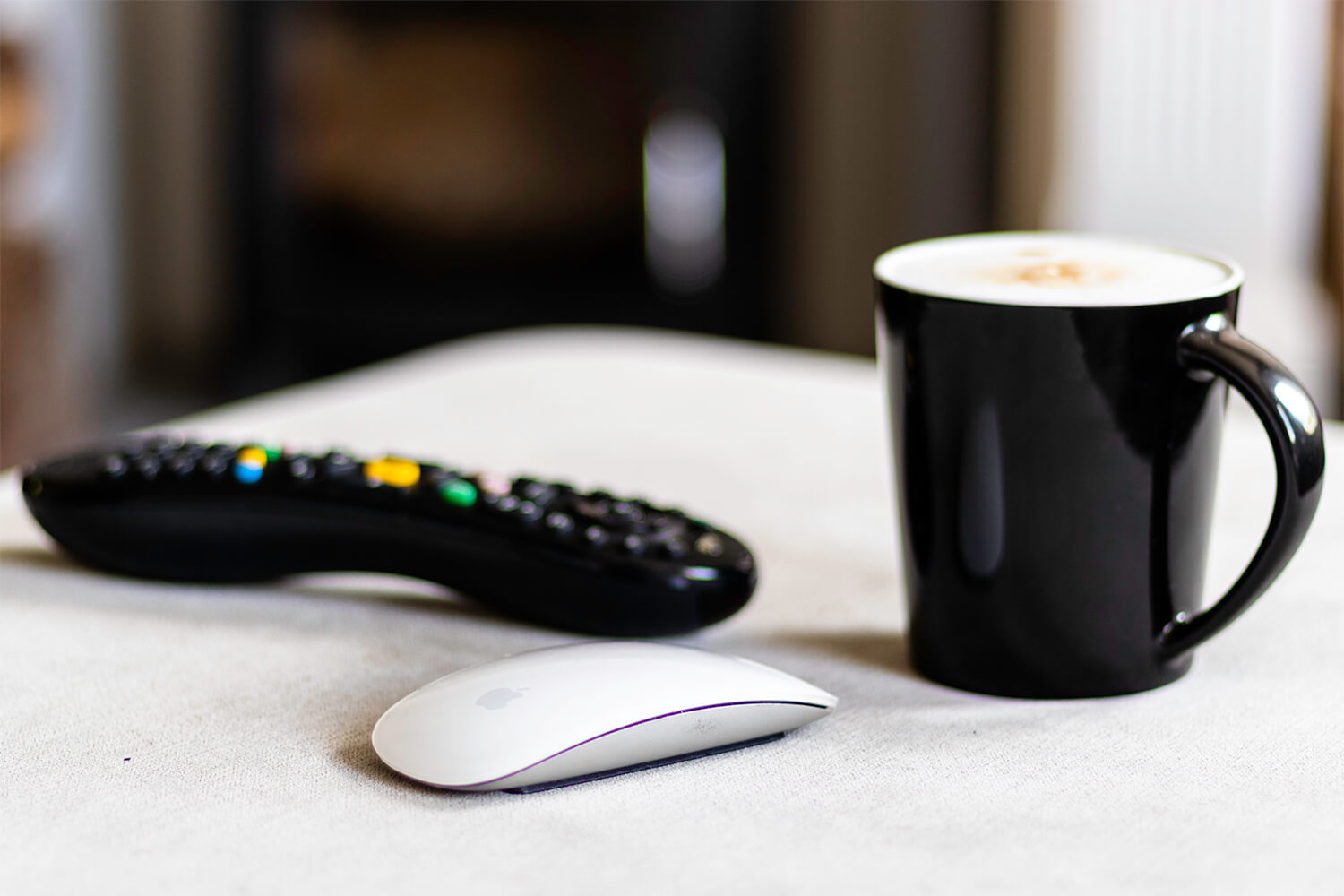 A magic mouse, cappucino and TV remote on a foot stool